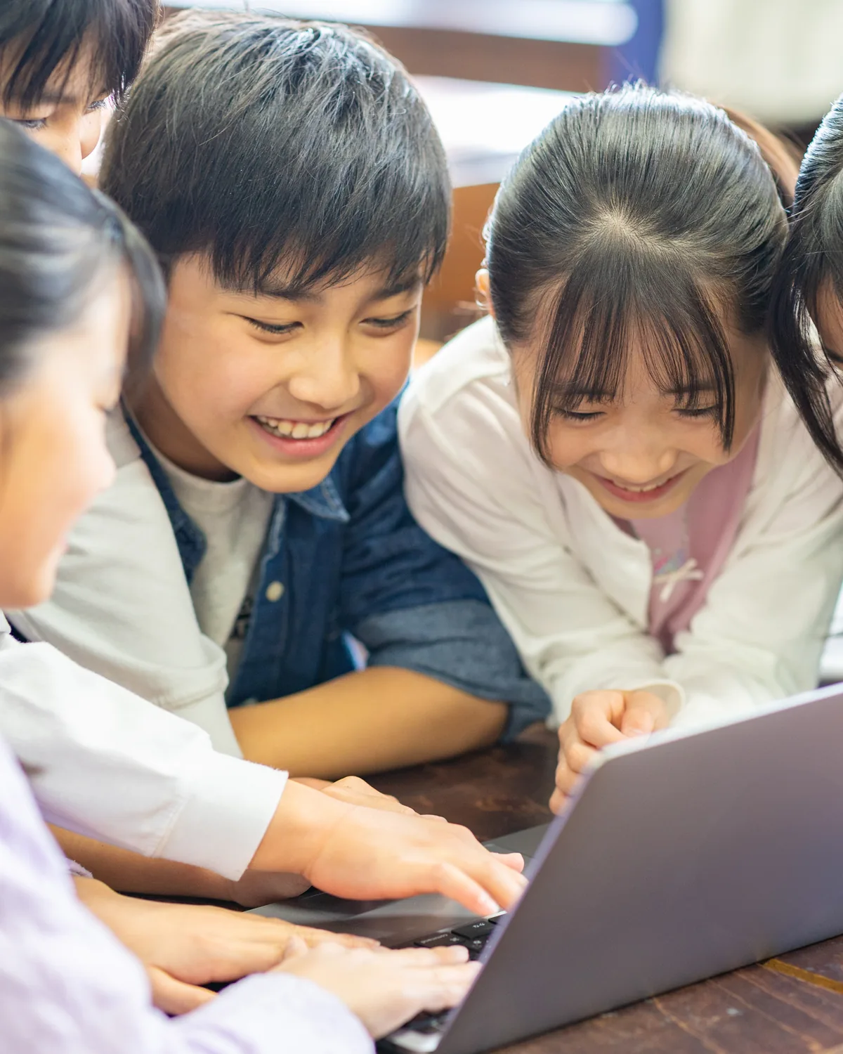 ノートパソコンを囲んでグループワークをする小学生たち